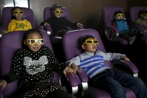 Children sit in purple movie-theater chairs, wearing disposable 3-D glasses.