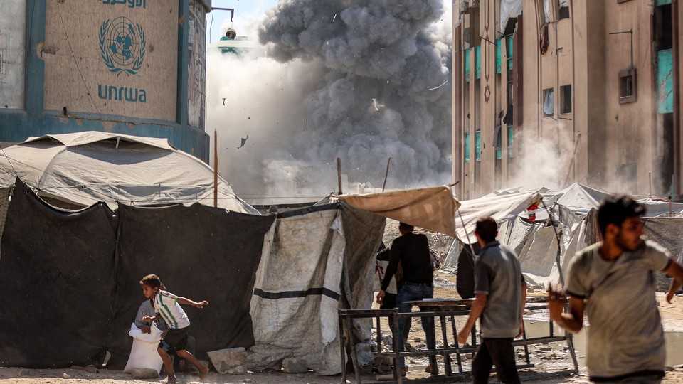 A street scene in Gaza shows billowing black smoke, a UN banner and people walking amid tents.