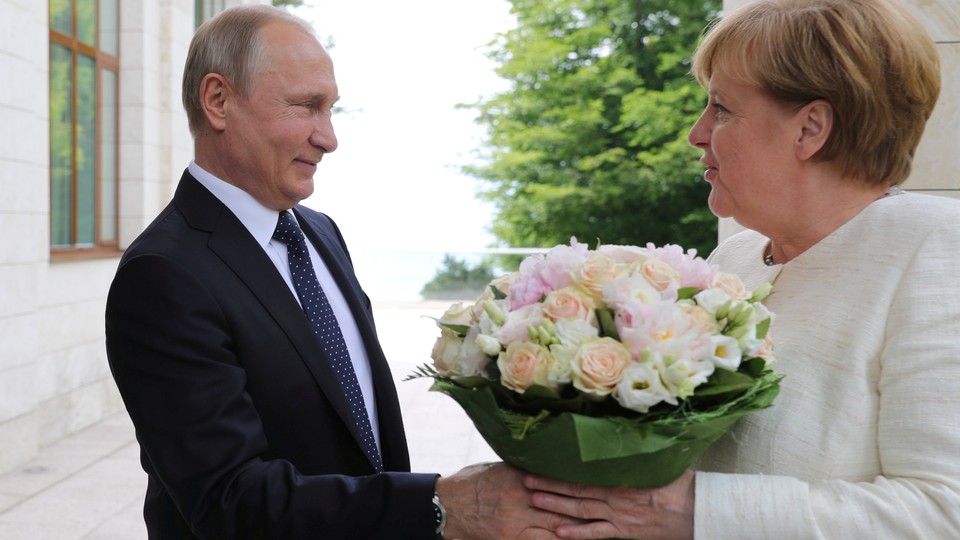 Putin hands Merkel a bouquet of flowers while shaking her hand at a meeting in Sochi.