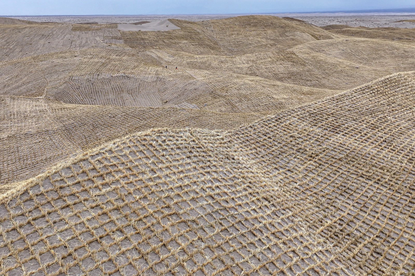 An aerial view of many sand dunes covered with a checkerboard pattern of straw planted in the sand.