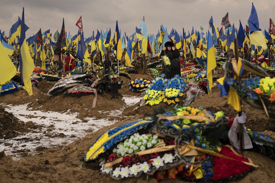 A woman walks through a cemetery, with graves covered by many wreaths and Ukrainian flags.