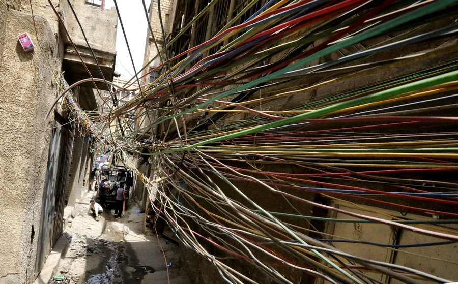 A huge tangle of electric wires hangs in an alley.