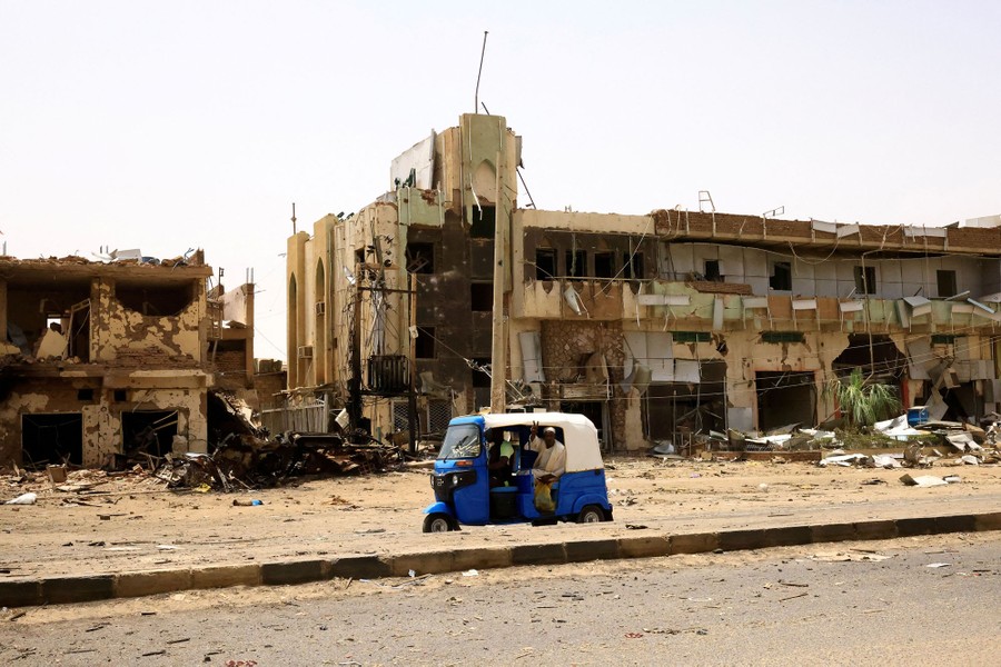 People pass by damaged cars and buildings.