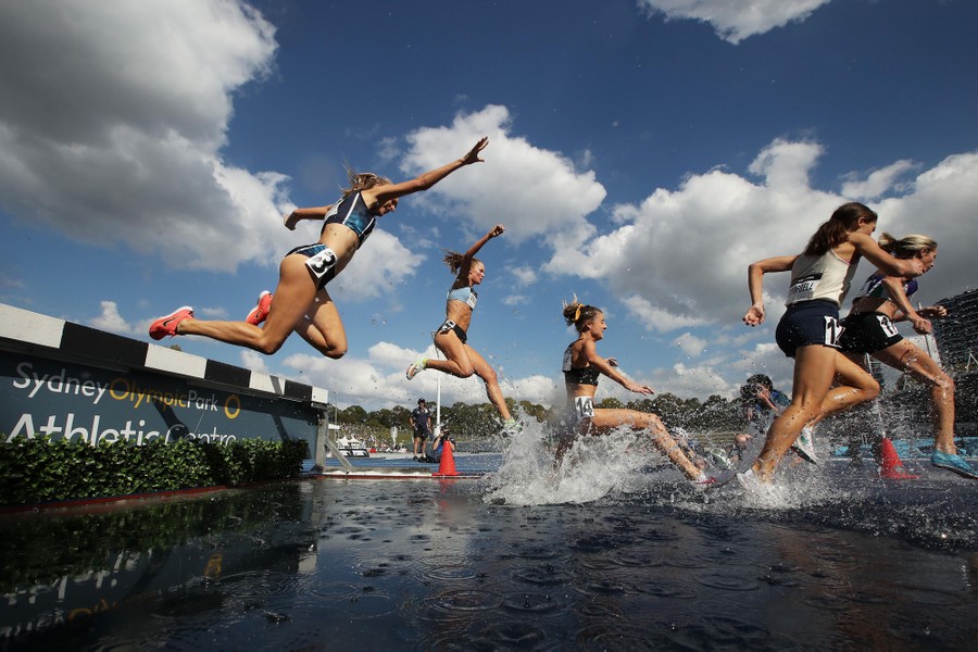 A runner falls as others splash in a water hazard during a race.