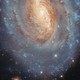 A telescopic view of a distant spiral galaxy with a yellowish center and more blue-colored star-forming regions toward the outer regions.