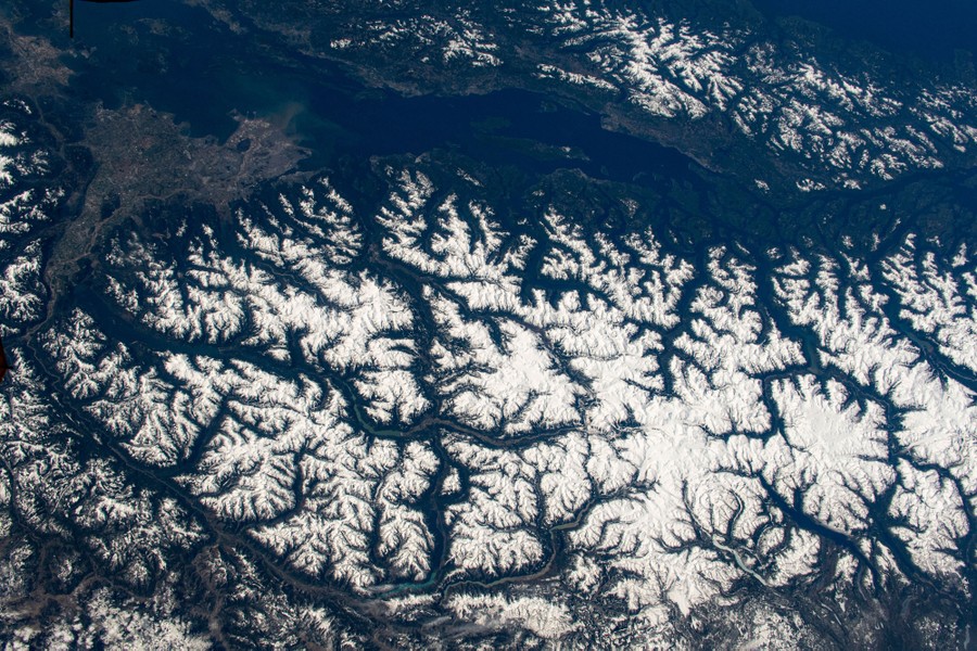 An aerial view of a textured landscape—many mountains and valleys outlined by snow and dark trees.