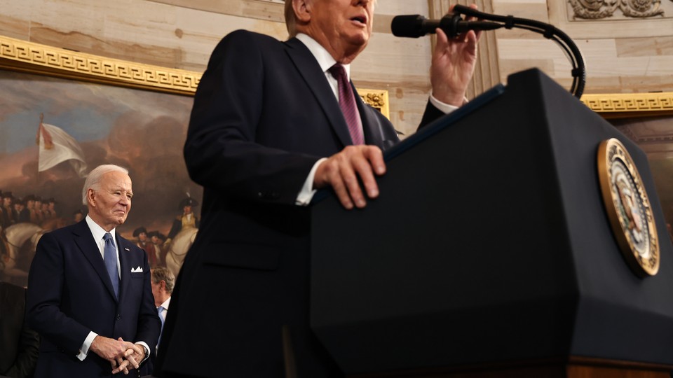 A photograph of Donald Trump speaking into a microphone, with Joe Biden in the background