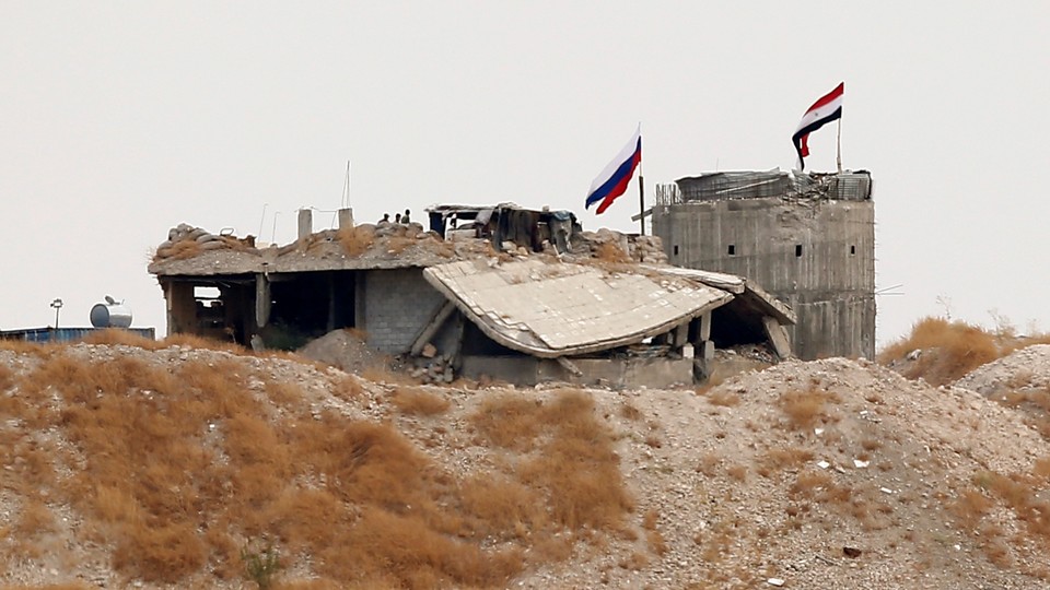 Russian and Syrian national flags are raised above a structure.