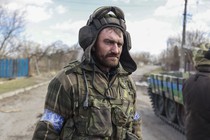 A soldier stands in a street near a tank.