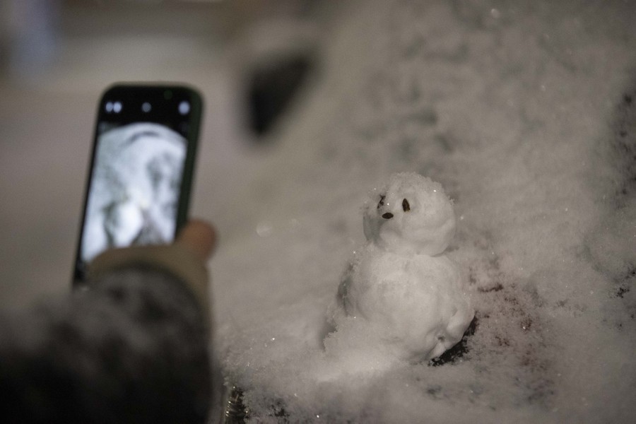 A person takes a photo of a tiny snowman.