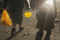 Two people walking in a park, carrying a yellow bag and a yellow leaf, photographed from behind