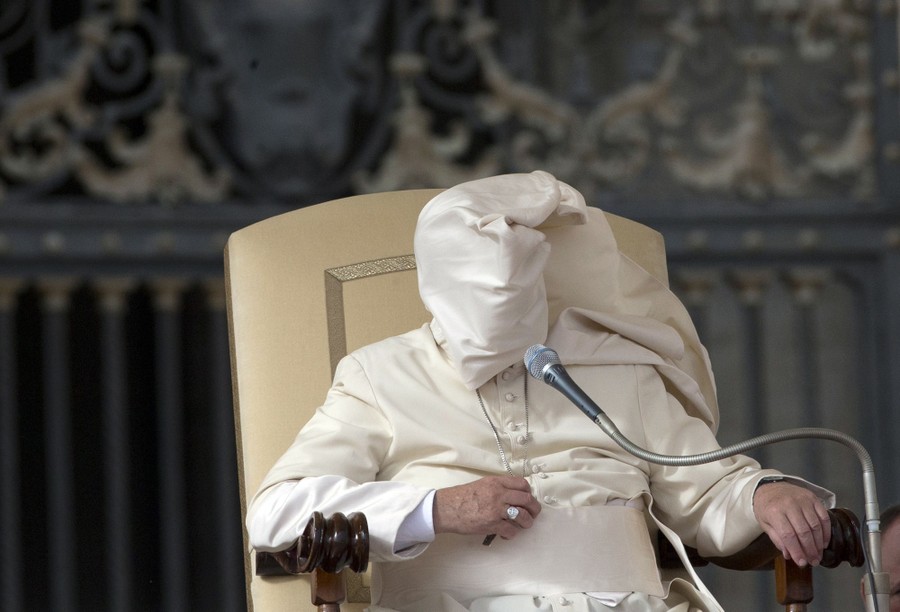 A gust of wind blows a loose part of Pope Francis’s clothing over his head and face.