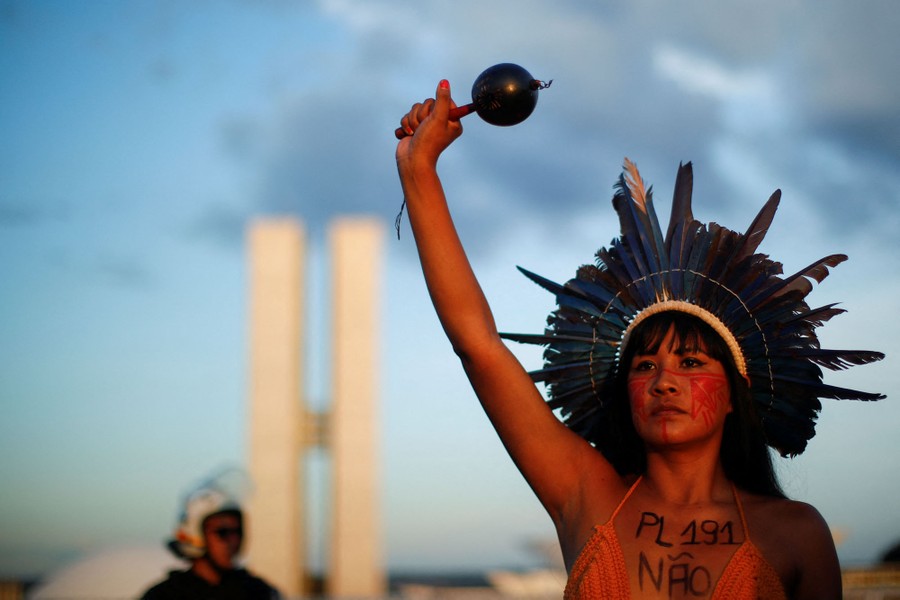 An indigenous protester wearing a feather headdress raises her arm during a protest.