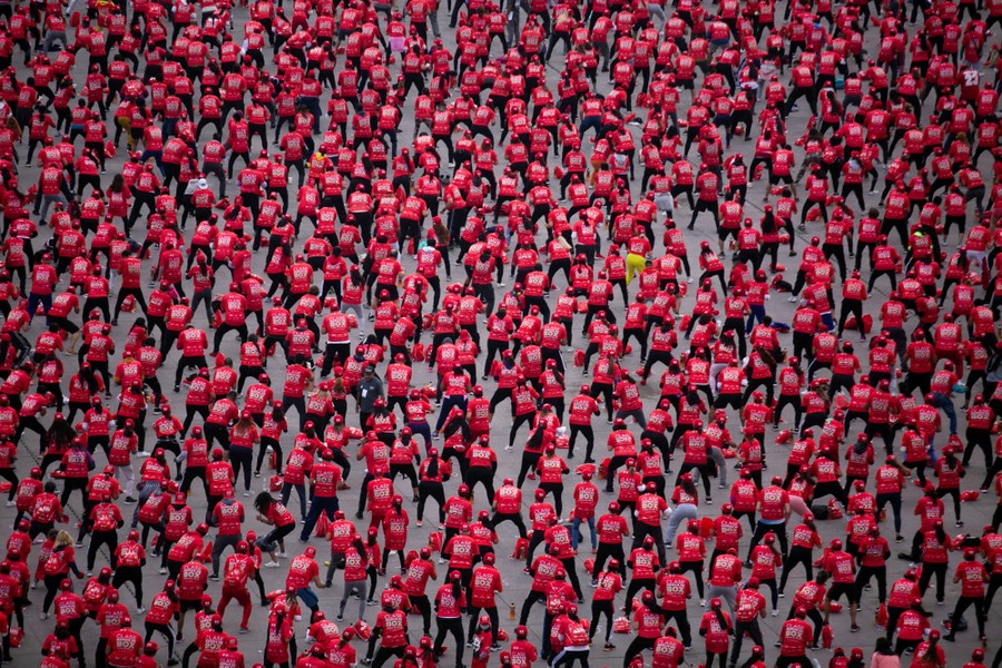 Hundreds of people wearing red shirts and hats exercise in a large open square.