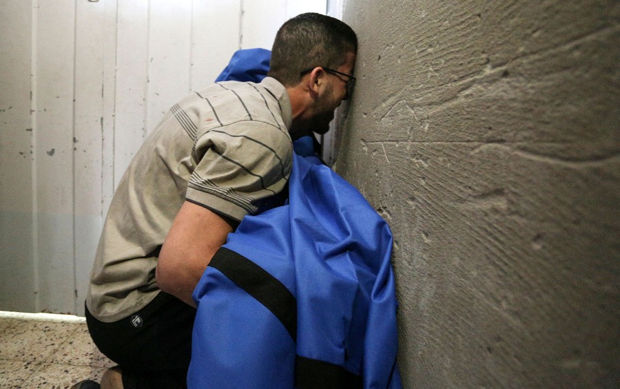 A distraught father leans his head against a wall as he holds the covered body of his daughter.