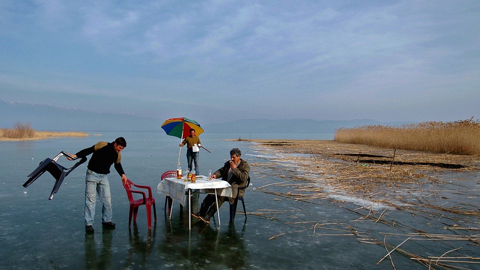 Three men set up a dining table in the middle of frozen water.