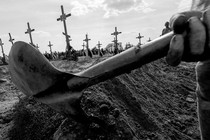 Black-and-white photo zooming in on a handheld digging tool, graves marked with crosses in the background