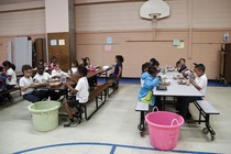 A group of children eats at two long lunch tables.