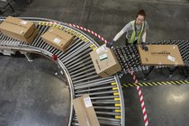 A worker loads Amazon packages onto a conveyor belt.