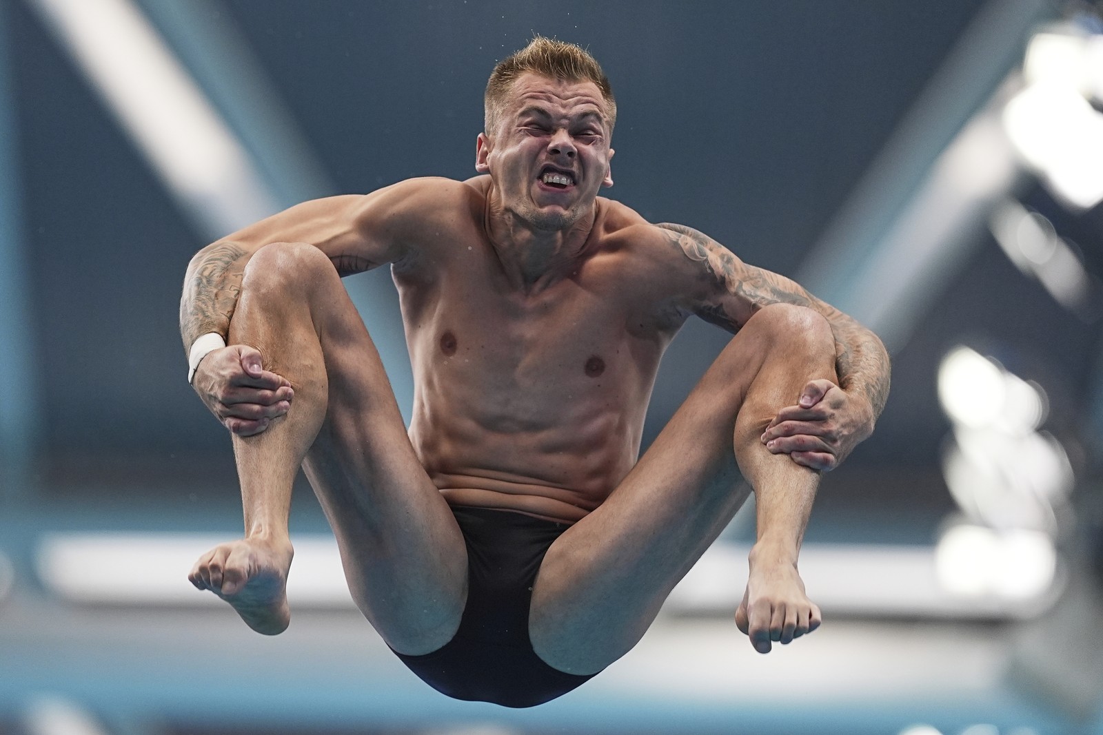 A diver's face is distorted as they tumble in the air during a diving competition.