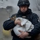 A rescue worker carries a cat wrapped in a towel.