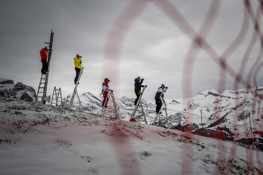 Five people stand atop stepladders set along a ski run.