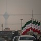 A hazy photograph of a street in Iran with a large skyscraper in the background and a number of Islamic Republic flags in the foreground