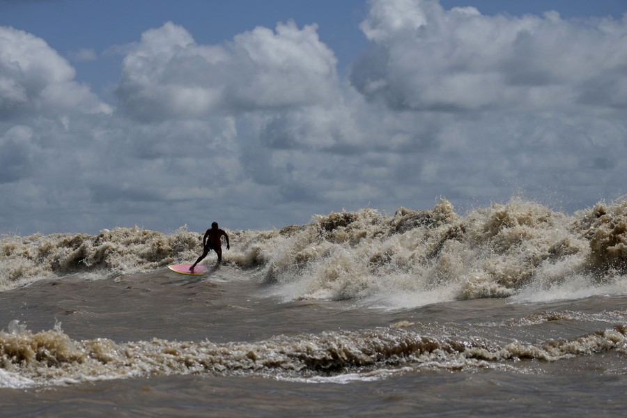 A surfer rides a turbulent wave in a river.