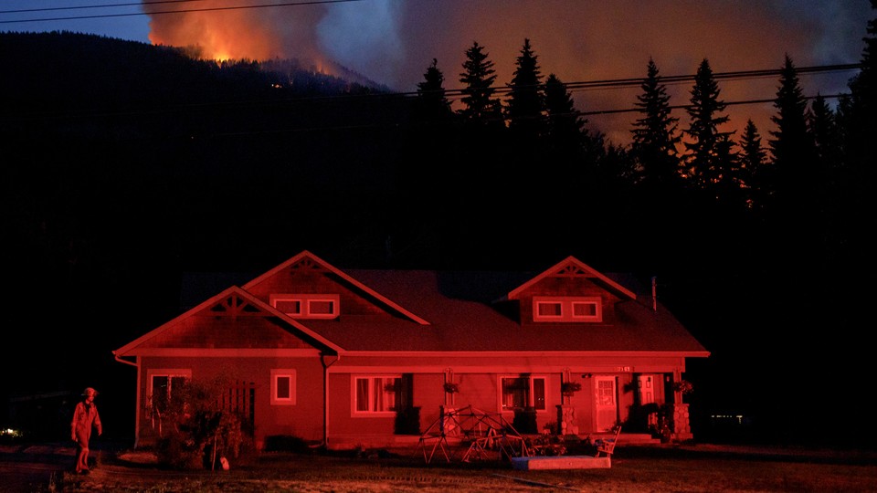 A house in Lytton glows red as a wildfire burns in the background.