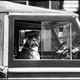 A black-and-white photograph of a boxer dog staring out a car window