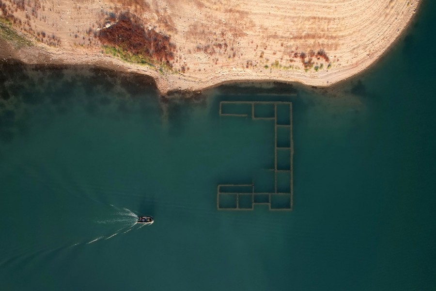 A view from the sky of a small boat on a lake, with the ruins of a structure visible near the water's surface.