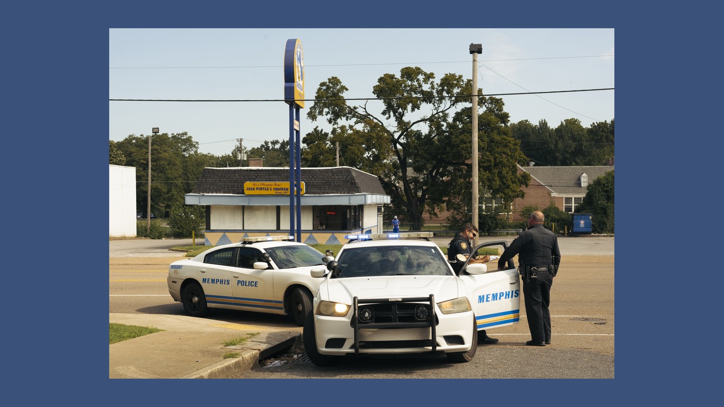 Two cops cars sit with doors open on a street corner, with cops outside