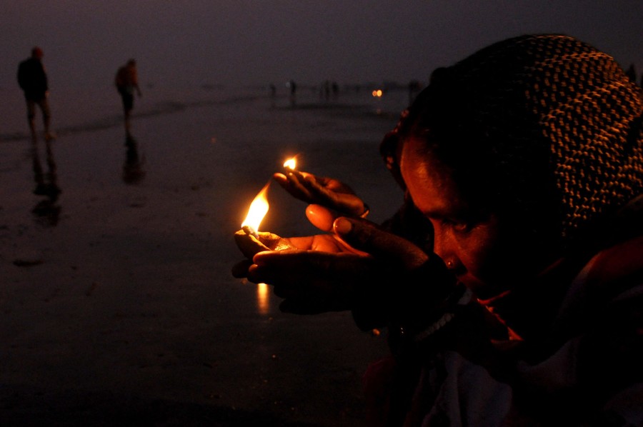People hold small lanterns near their faces on a riverbank.
