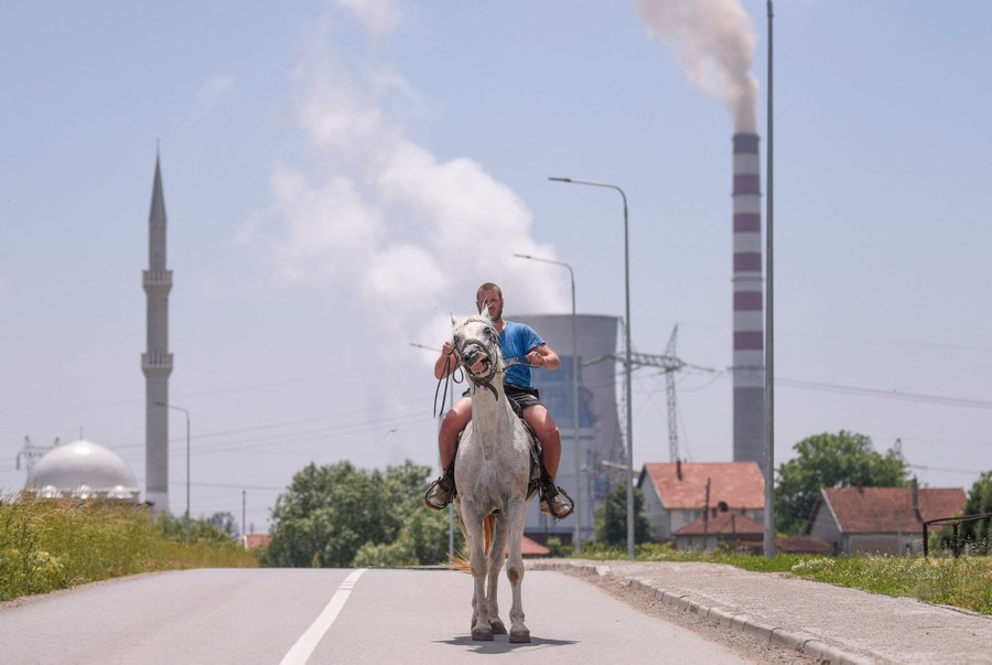 A man rides his horse near a coal-fired power plant.
