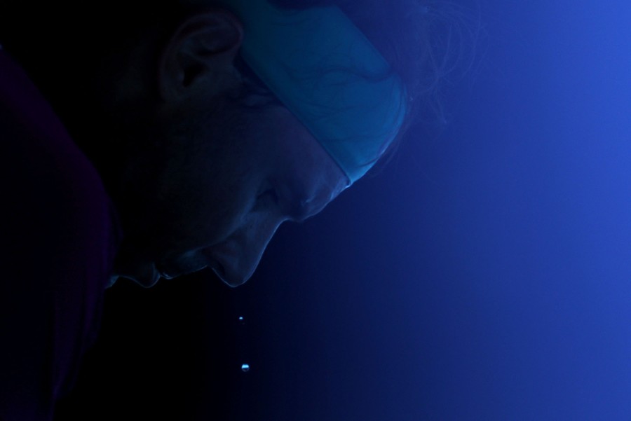 A close view of a tennis player who is leaning over with sweat dripping off his face.