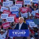 Donald Trump speaks at a rally in front of a sea of signs that say: WITCH HUNT and TRUMP 2024