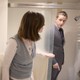 A woman peeking in on James Hamblin, who is fully dressed in a suit, in the shower