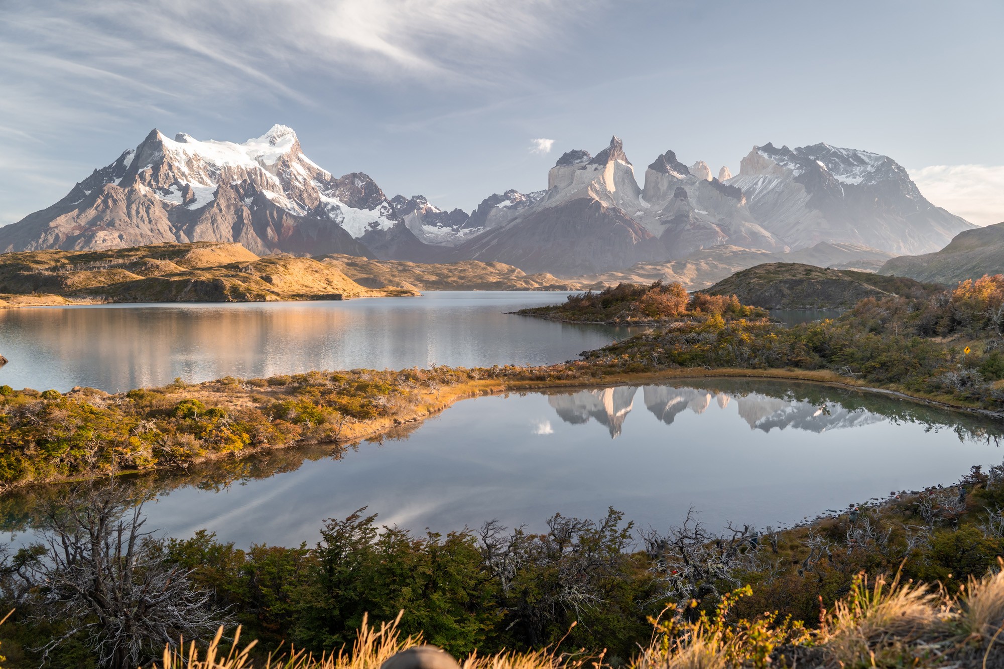 A landscape image of distant, tall mountains seen beyond hills and lakes.