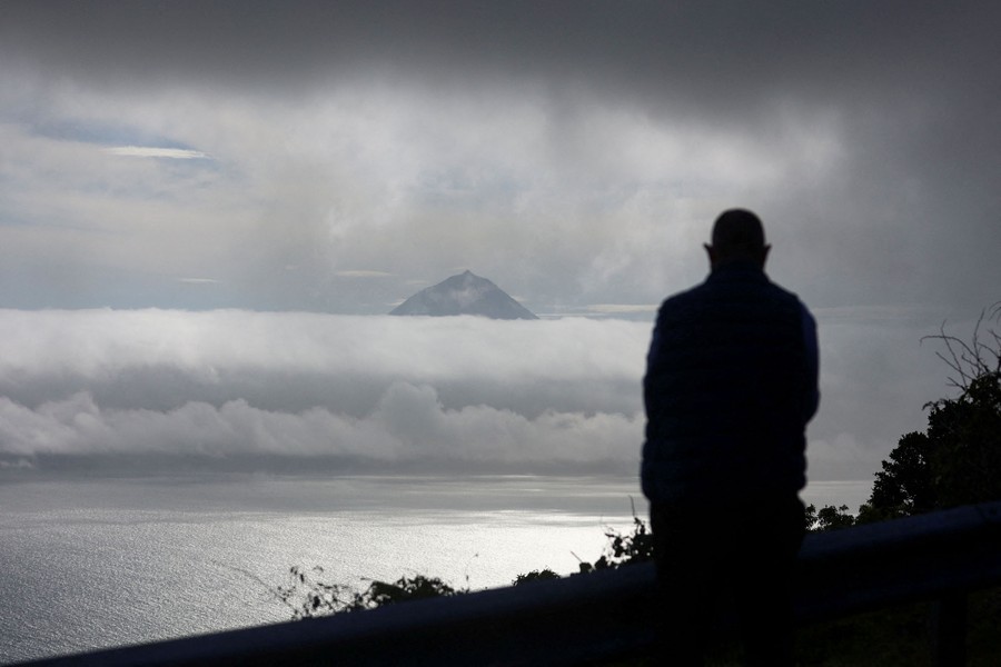 A silhouette of a person looking out over clouds, the ocean, and a distant island.
