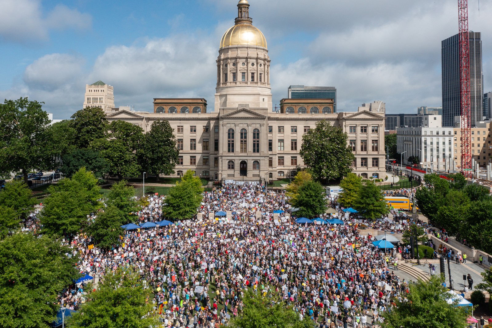 A crowd of demonstrators gathers in open space in front of a state capitol building.