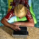 A photo of a man in a pool working on a laptop at the edge of the water.