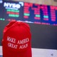 A red MAGA cap in front of a declining stock-market screen