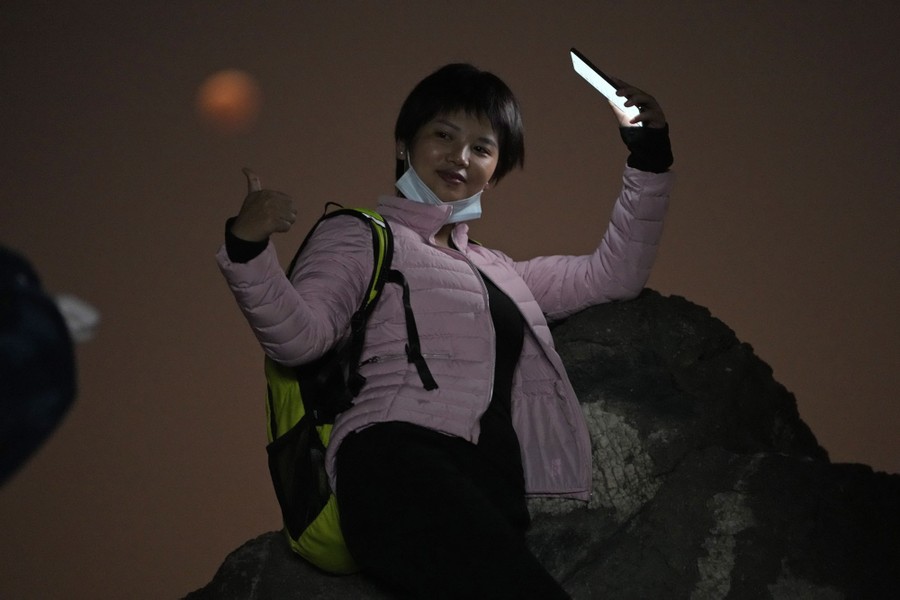 A woman poses for a photo beneath an eclipsed moon.