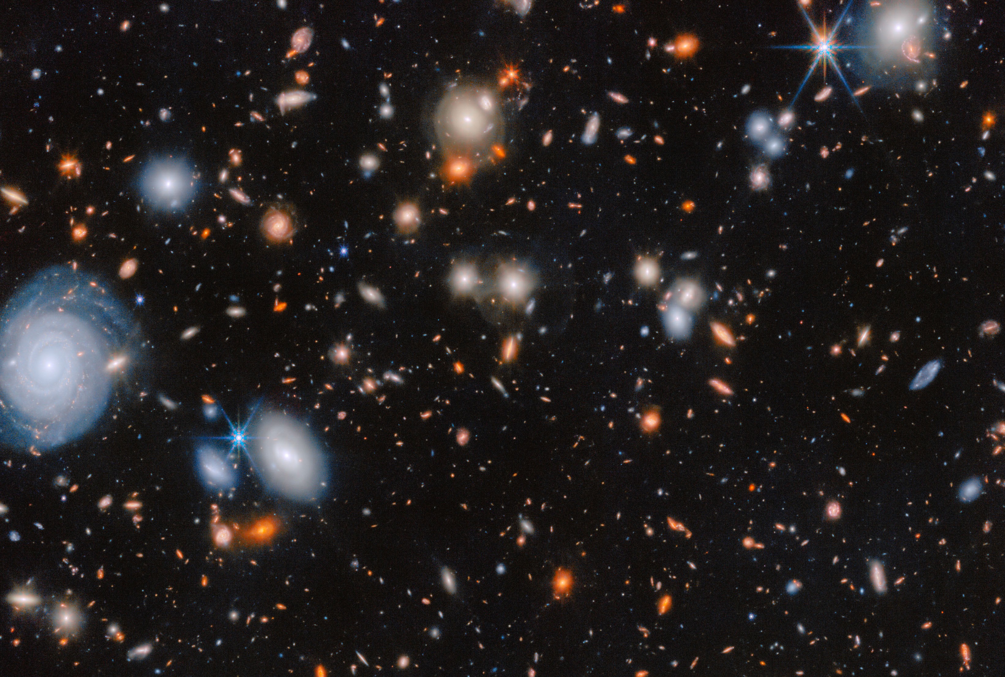 An image of many glowing galaxies in deep space, in various shapes and colours, on a black background