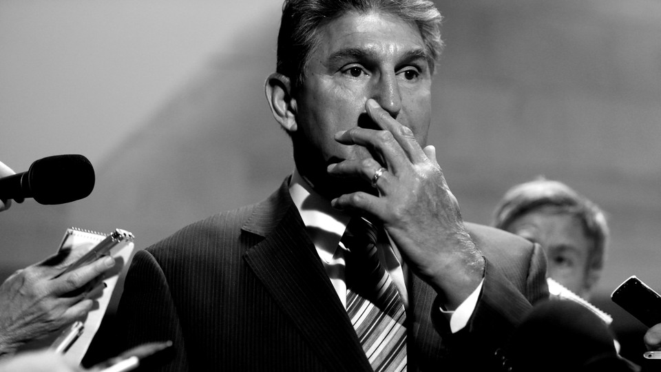 Joe Manchin stands amid reporters, covering his mouth with his hand.