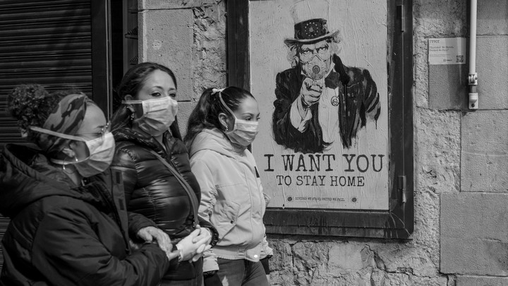 Women wearing face masks passing by a sign a poster which says "I want you to stay home."