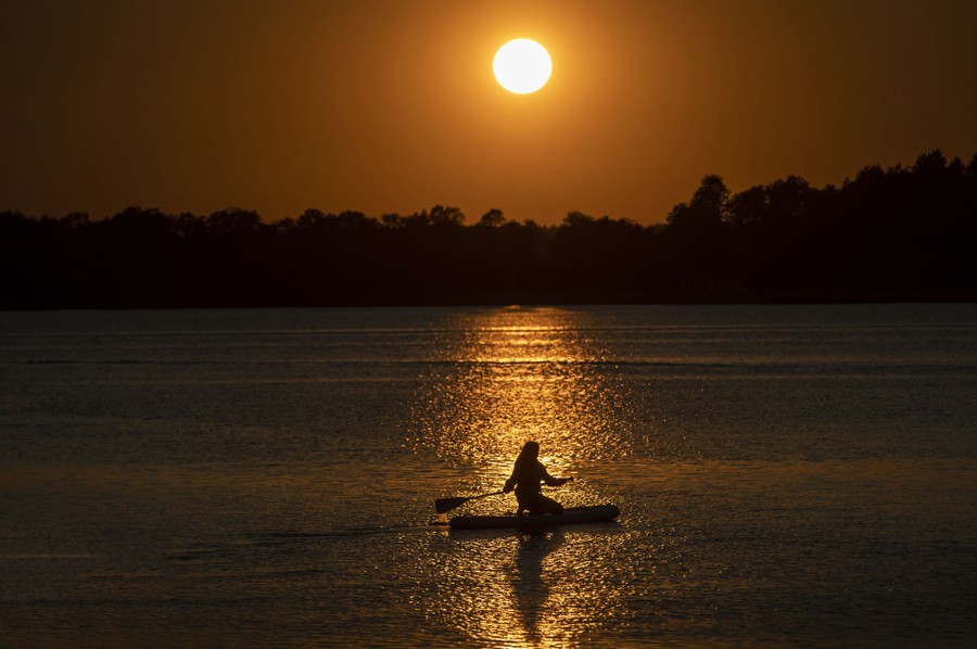 A person steers a board on a lake during sunset.
