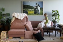 A child stands on a table, staring at a recently-made pillow fort.