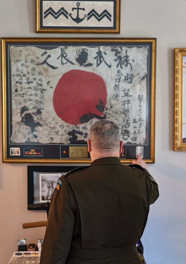 A photograph of a man standing in front of framed World War II artifact. 