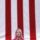 A color photo of Pam Bondi speaking in front of a large, vertical American flag.